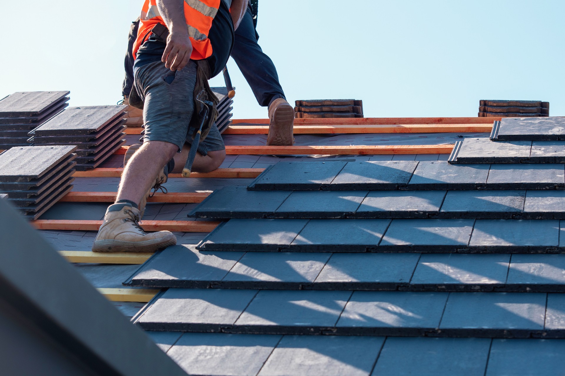 Builder carefully places roof tiles on a sloped surface while standing on top of a building showcasing the effort involved in roofing work
