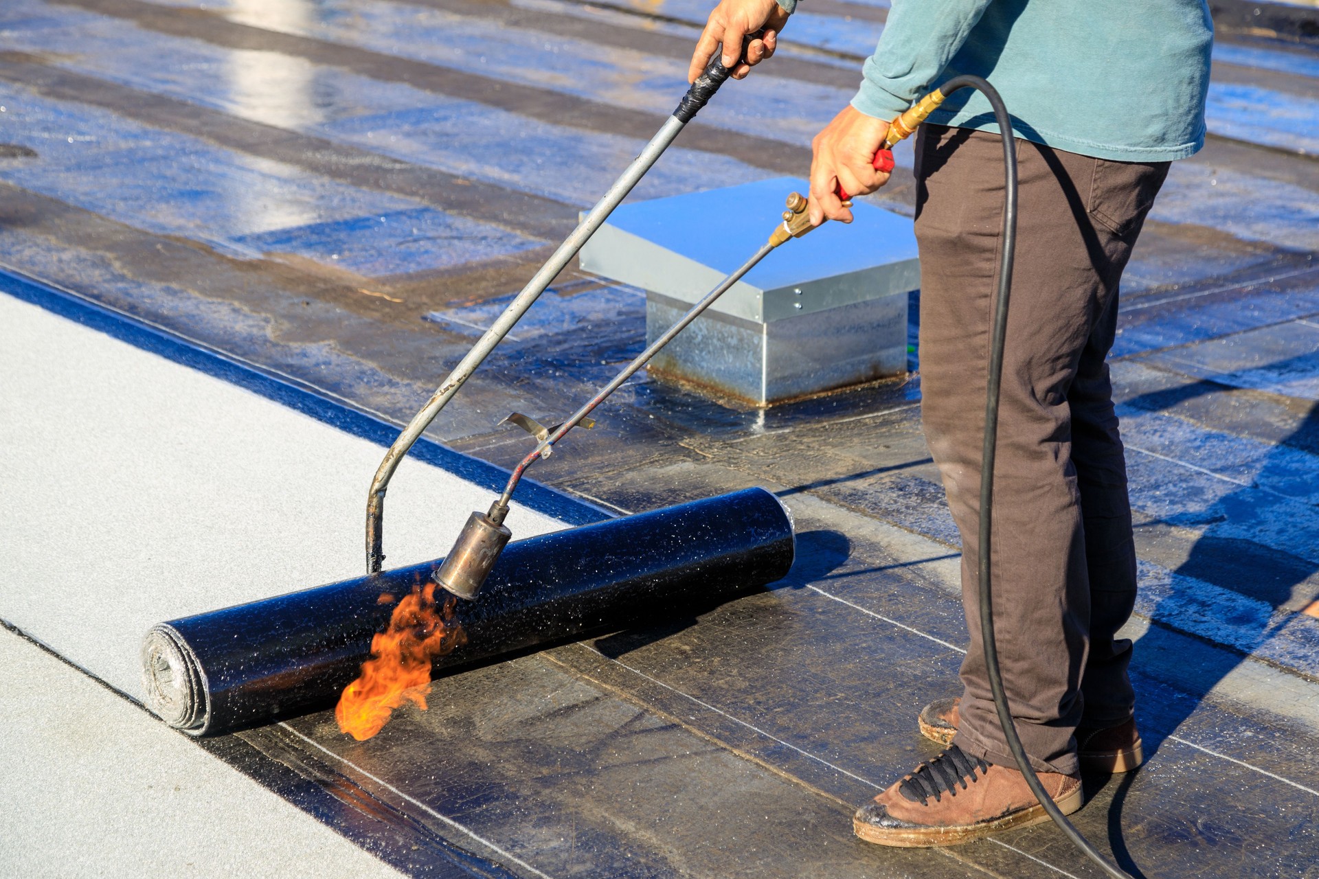 Roofer applying torch to bitumen membrane on torch down roof