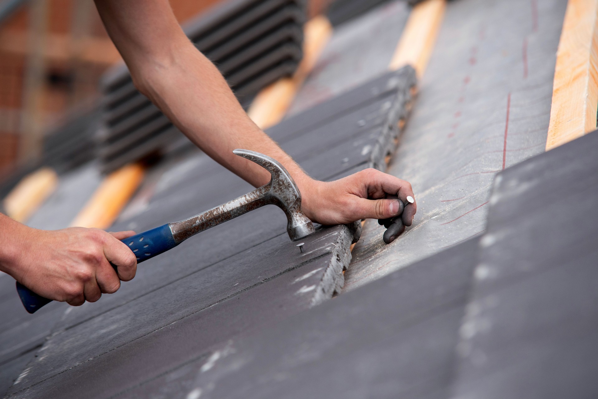 Close-up of skilled builder hands carefully placing roofing tiles on sloped surface of building and using hammer to ensure proper alignment